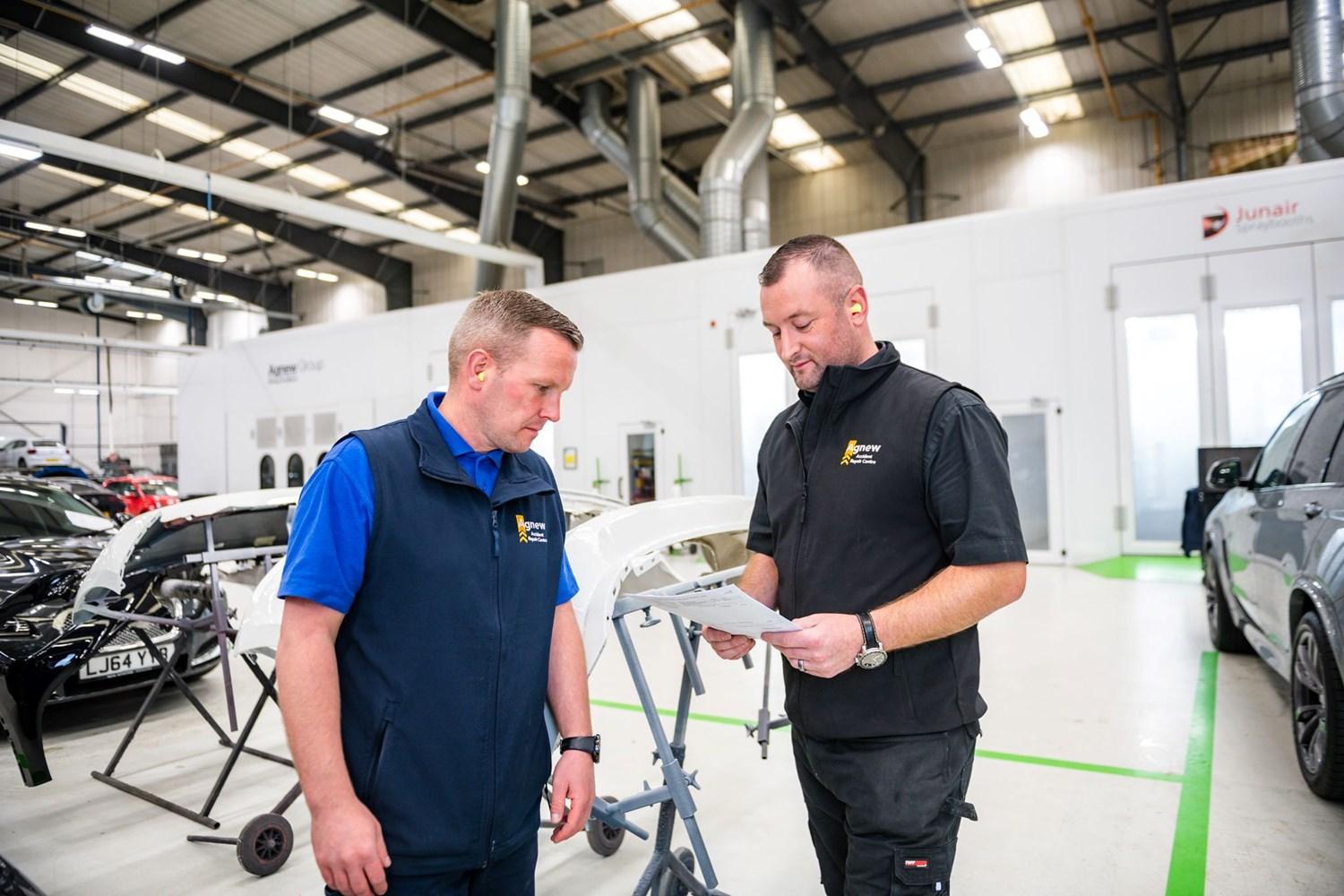 Two Agnew Repair Centre Repair Specialists discuss list of repairs to be made to a vehicle at the Agnew Repair Centre workshop, Belfast, Northern Ireland.