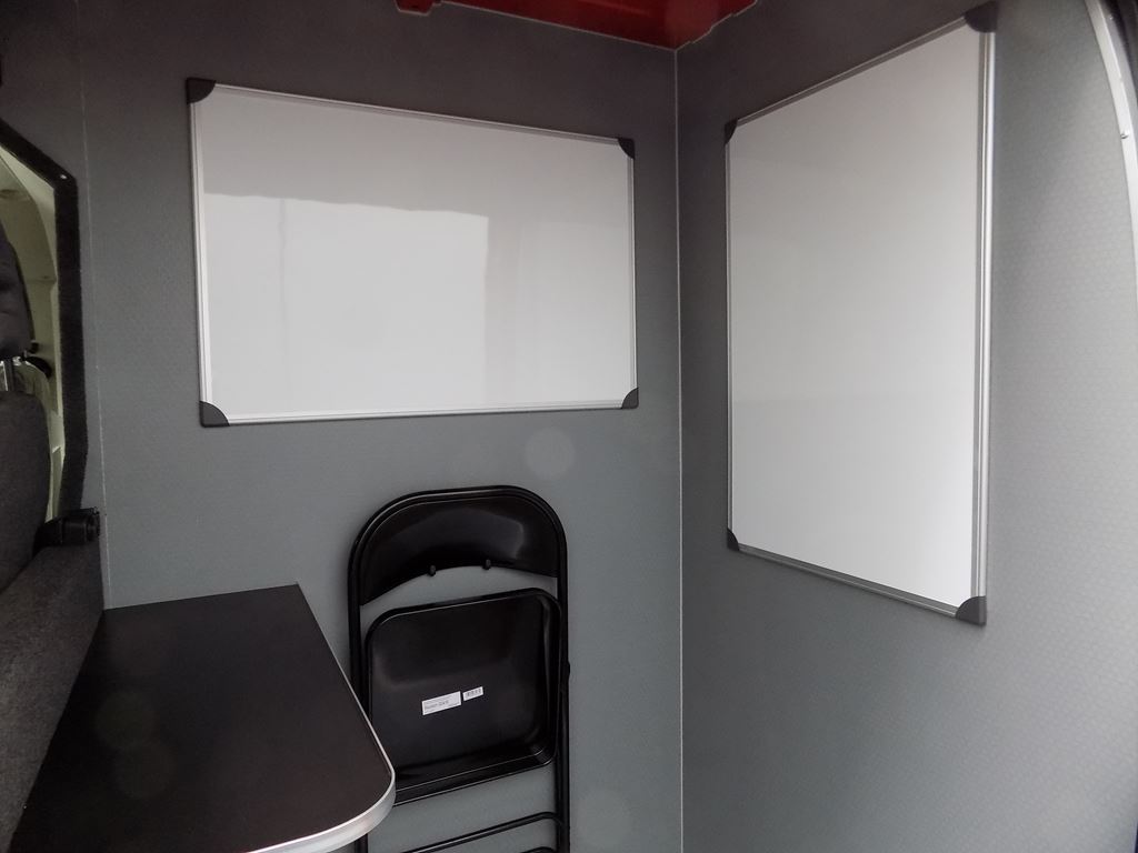 Work van interior with desk edge, folding chair and whiteboards for planning.