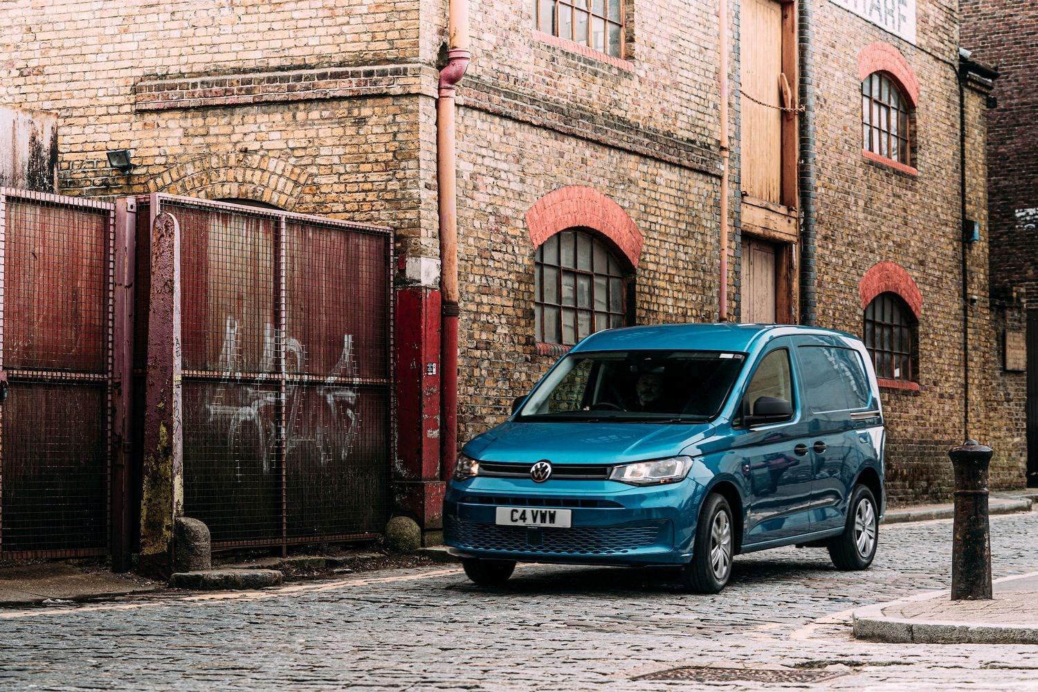 Blue Volkswagen Caddy parked on a city street with red brick building and cobbled streets.