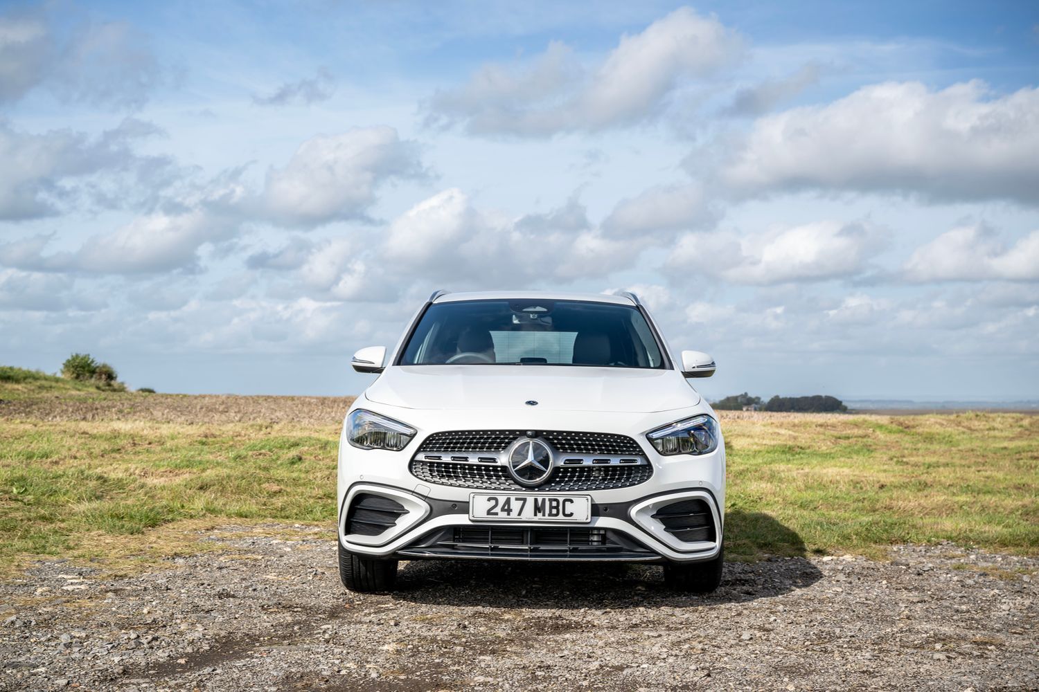 The front end of a white Mercedes-Benz GLA parked in a field.