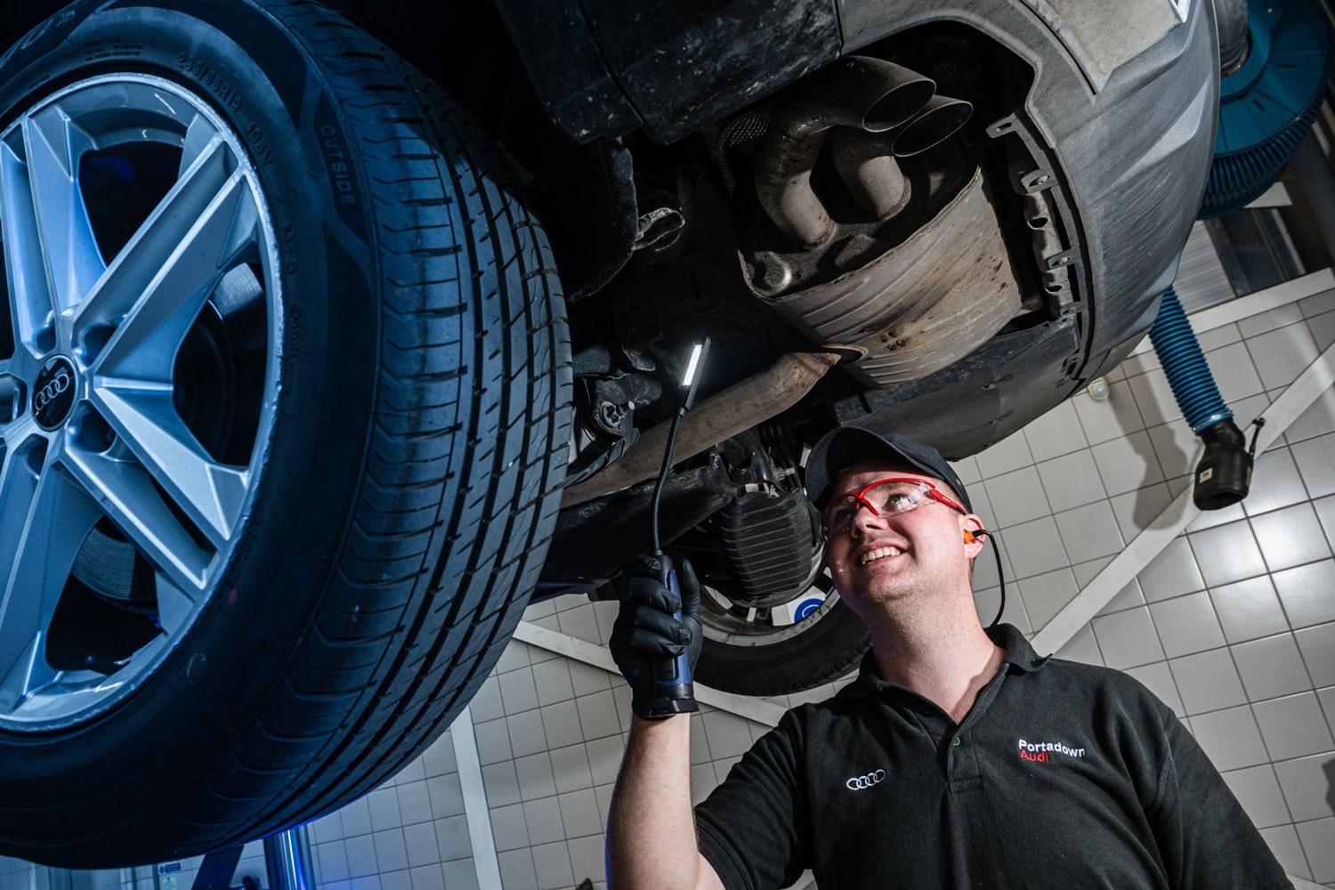 Audi Repair Specialist checks the undercarriage of an Audi A3 with a handheld light during repair