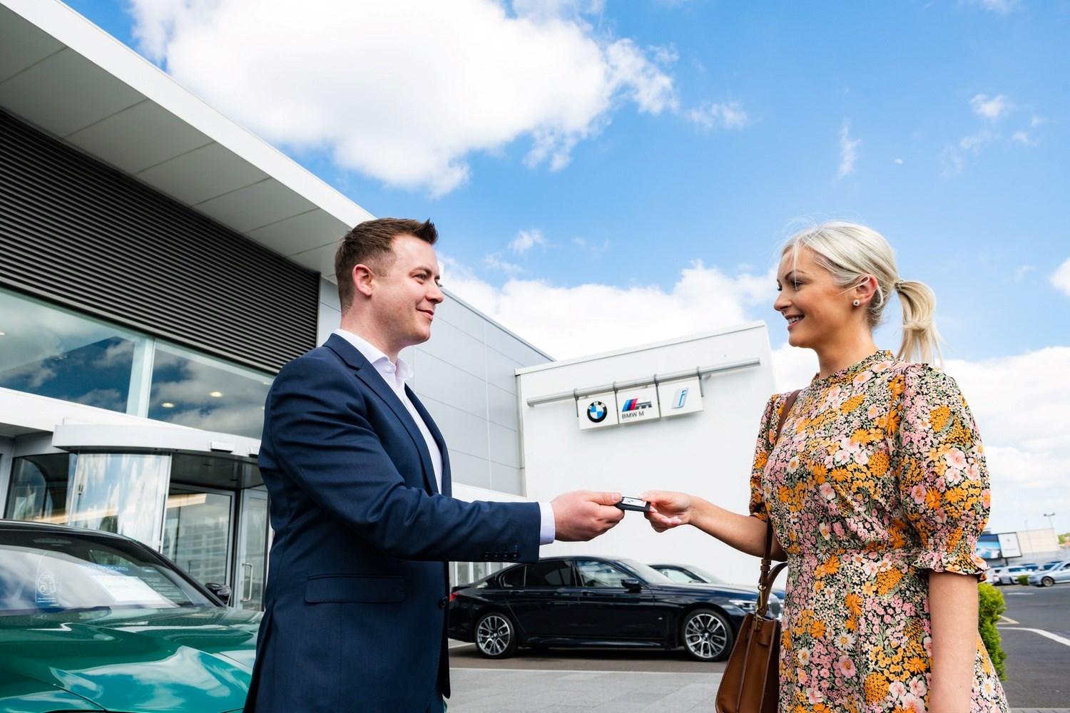 Bavarian BMW Sales Specialist talks hands over keys to customer to their new BMW outside of the Bavarian BMW showroom.