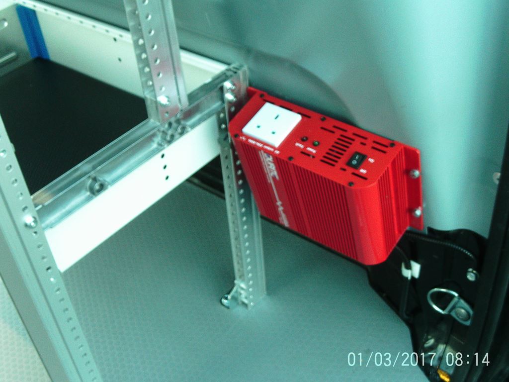 Red power inverter unit mounted to the van side wall near the racking frame.