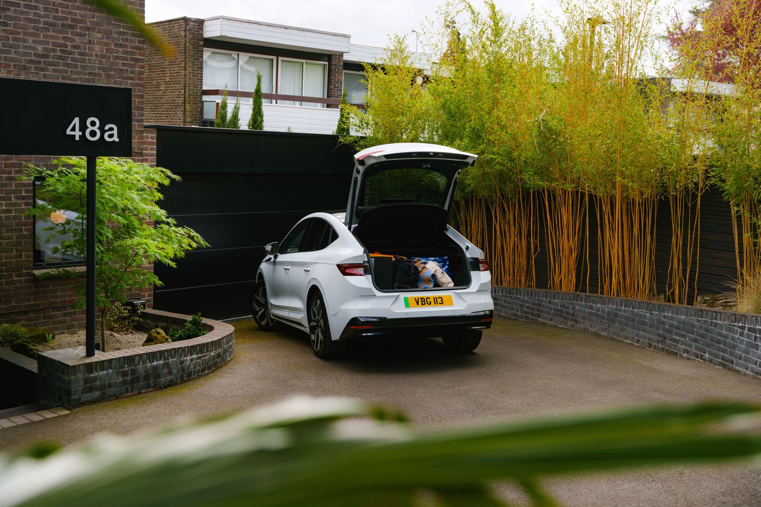 Rear view of the Skoda Enyaq Coupe with boot open, parked outside home.