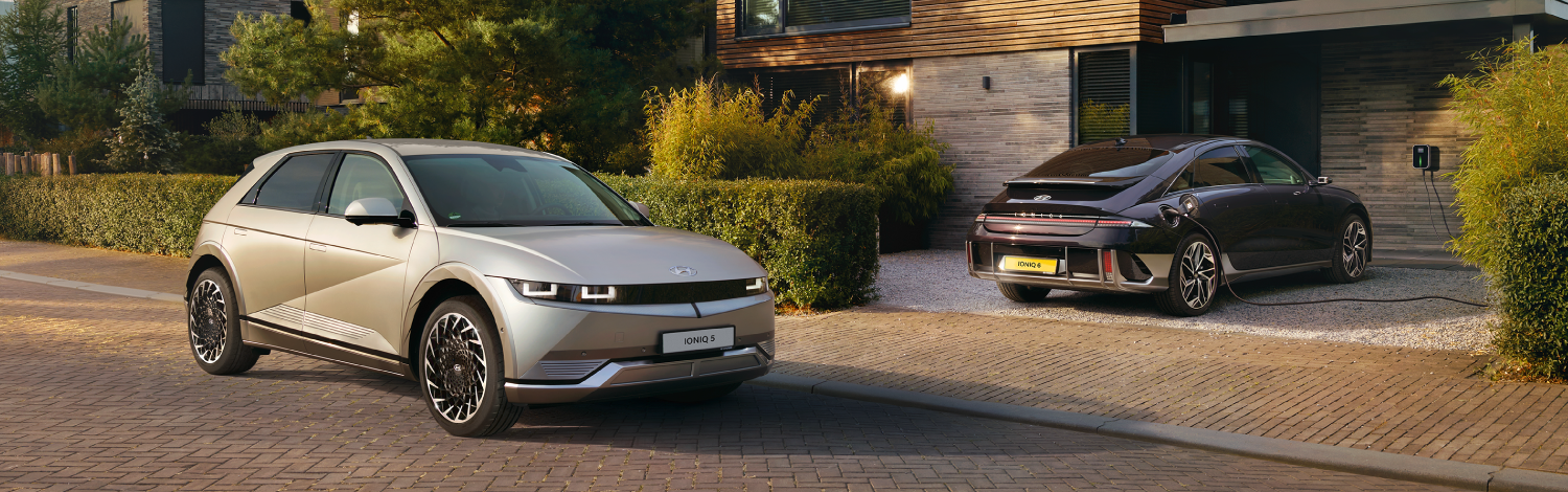 Silver Hyundai IONIQ 5 on the left and a black Hyundai IONIQ 6 charging in front of a house on the right