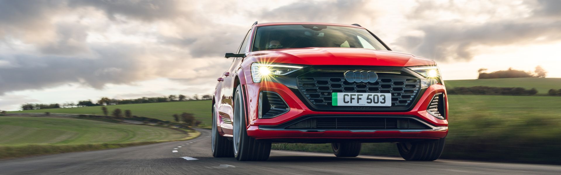 Front view of red Audi SQ8 e-tron as it drives on country road with hills in background