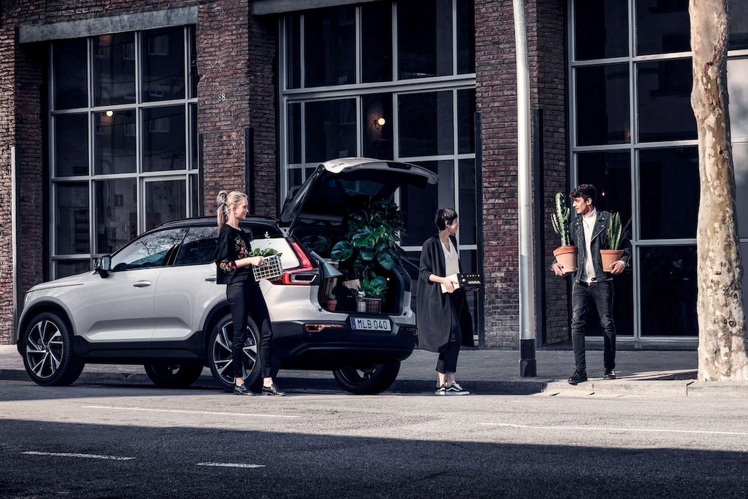 Family moving into a new city apartment are carrying items out of a parked Volvo XC90 Recharge