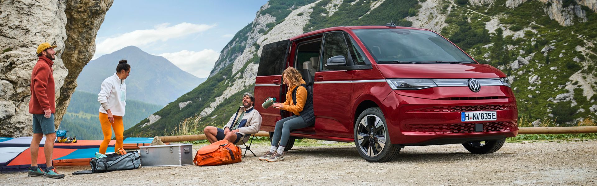The new Volkswagen Multivan, available at Agnew Van Centre. The Multivan is parked on a rocky beach with friends gathered outside with camping gear.
