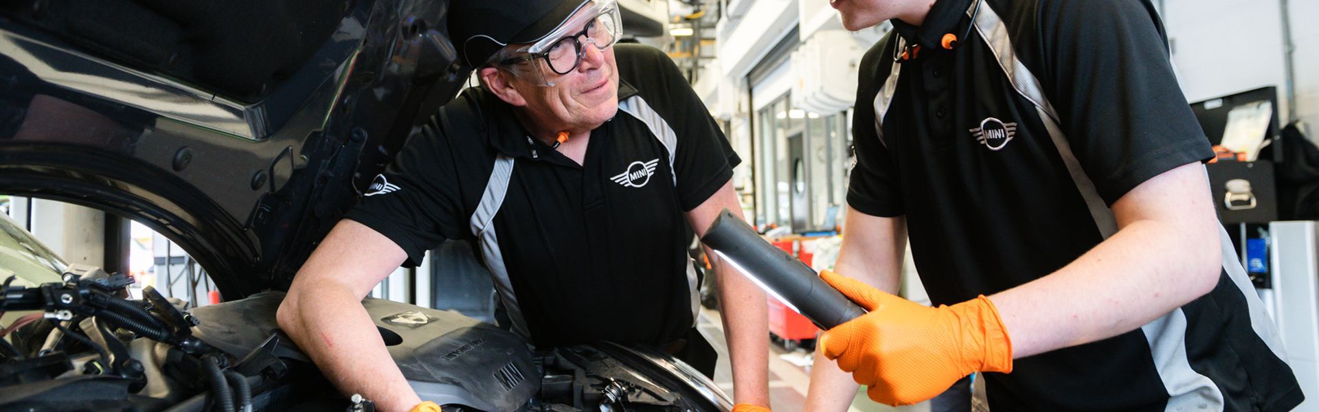 Two MINI Repair Specialists talk to each other during an under the hood inspection at the MINI Repair Centre at Bavarian MINI