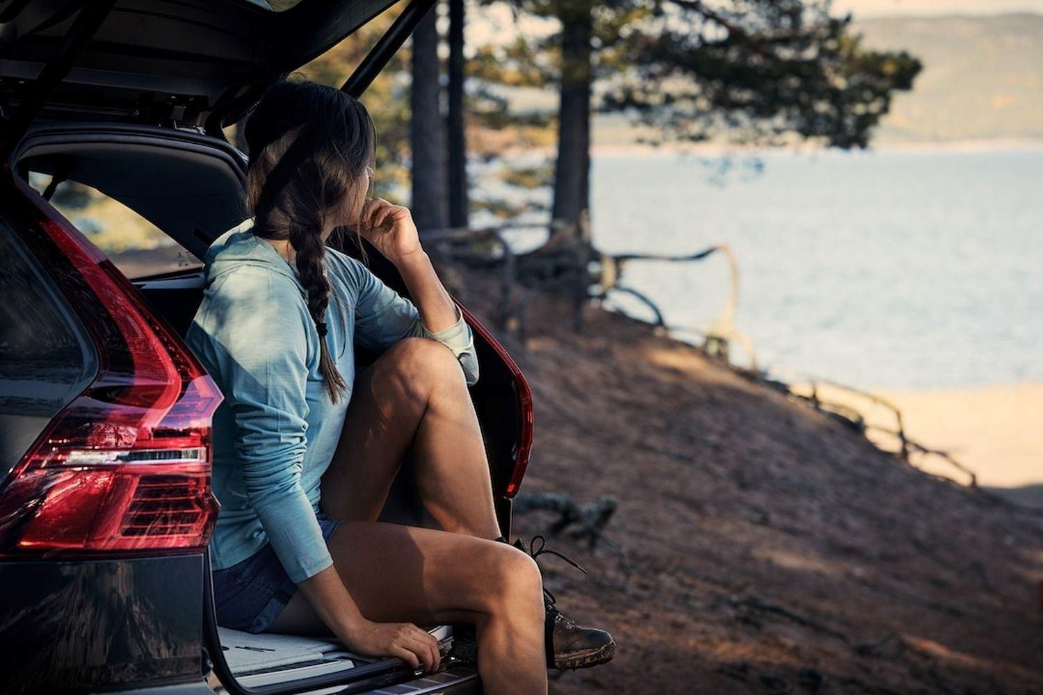 Person sits in the boot of thier Volvo vehicle while looking out towards beach