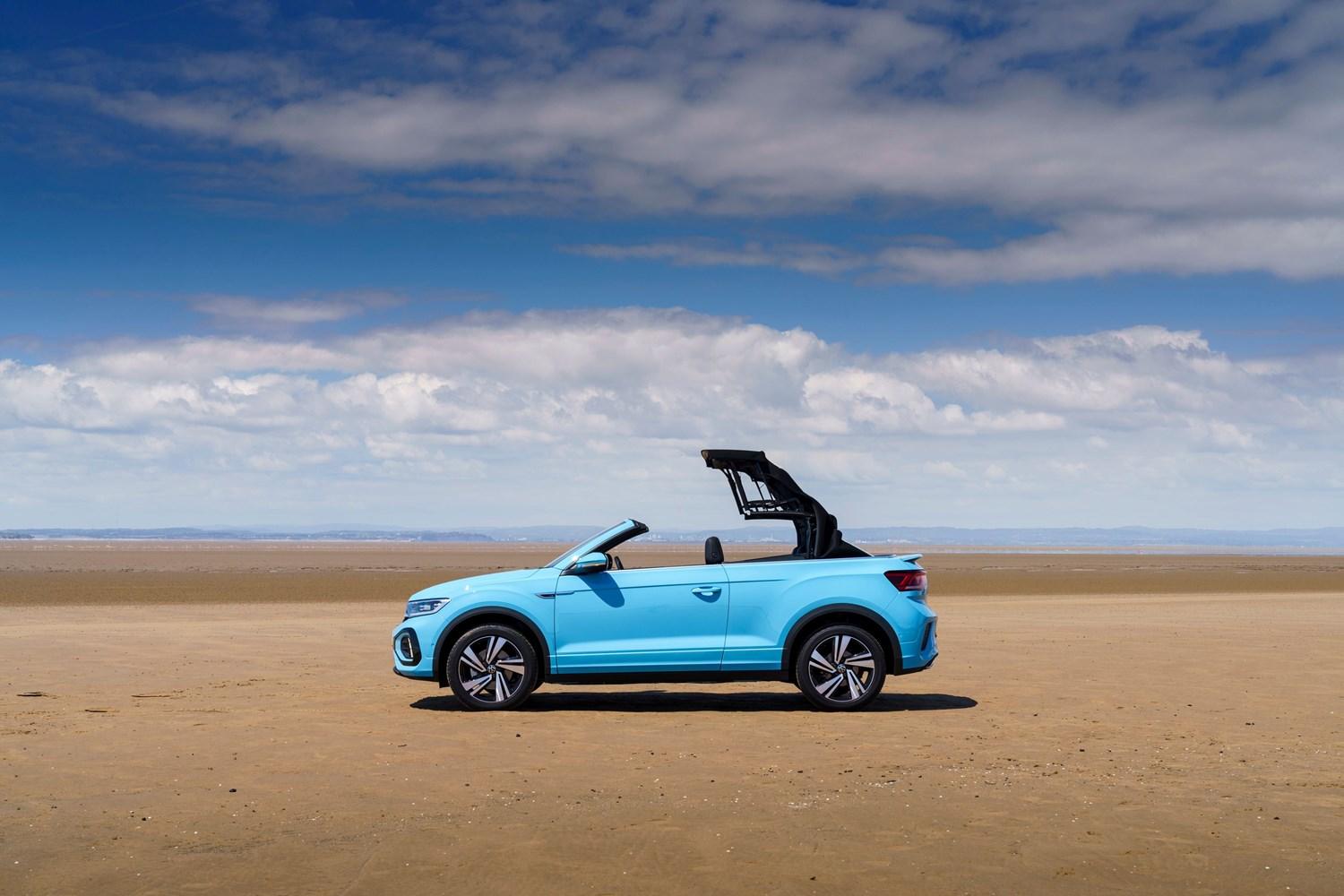 Side view of the new Volkswagen T-Roc Cabriolet in blue, parked on beach with sunroof going down