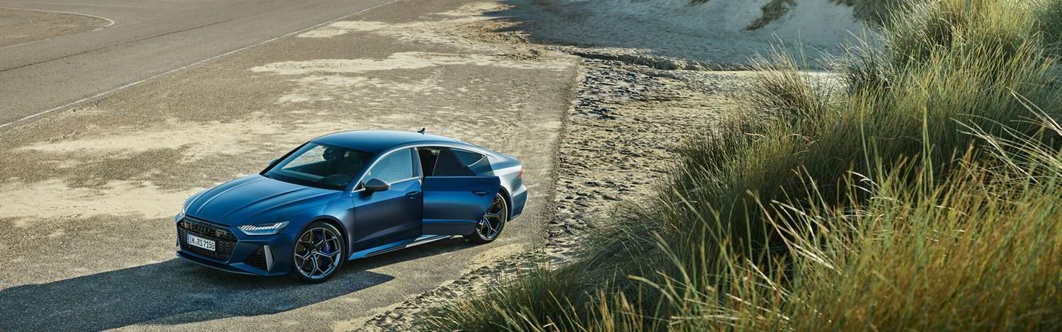 Audi e-tron GT quattro is parked at the edge of a sandy beach with sea visible behind