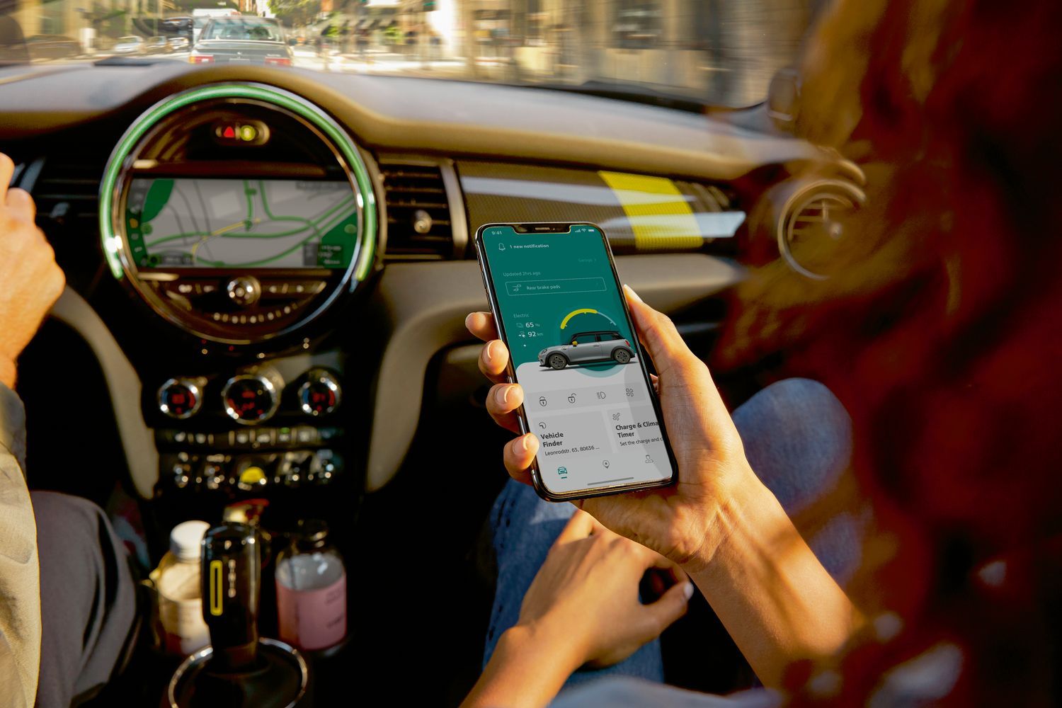 Interior view of the new MINI Electric, close-up of the central infotainment system with passenger using the myMINI App to find out more about the vehicle