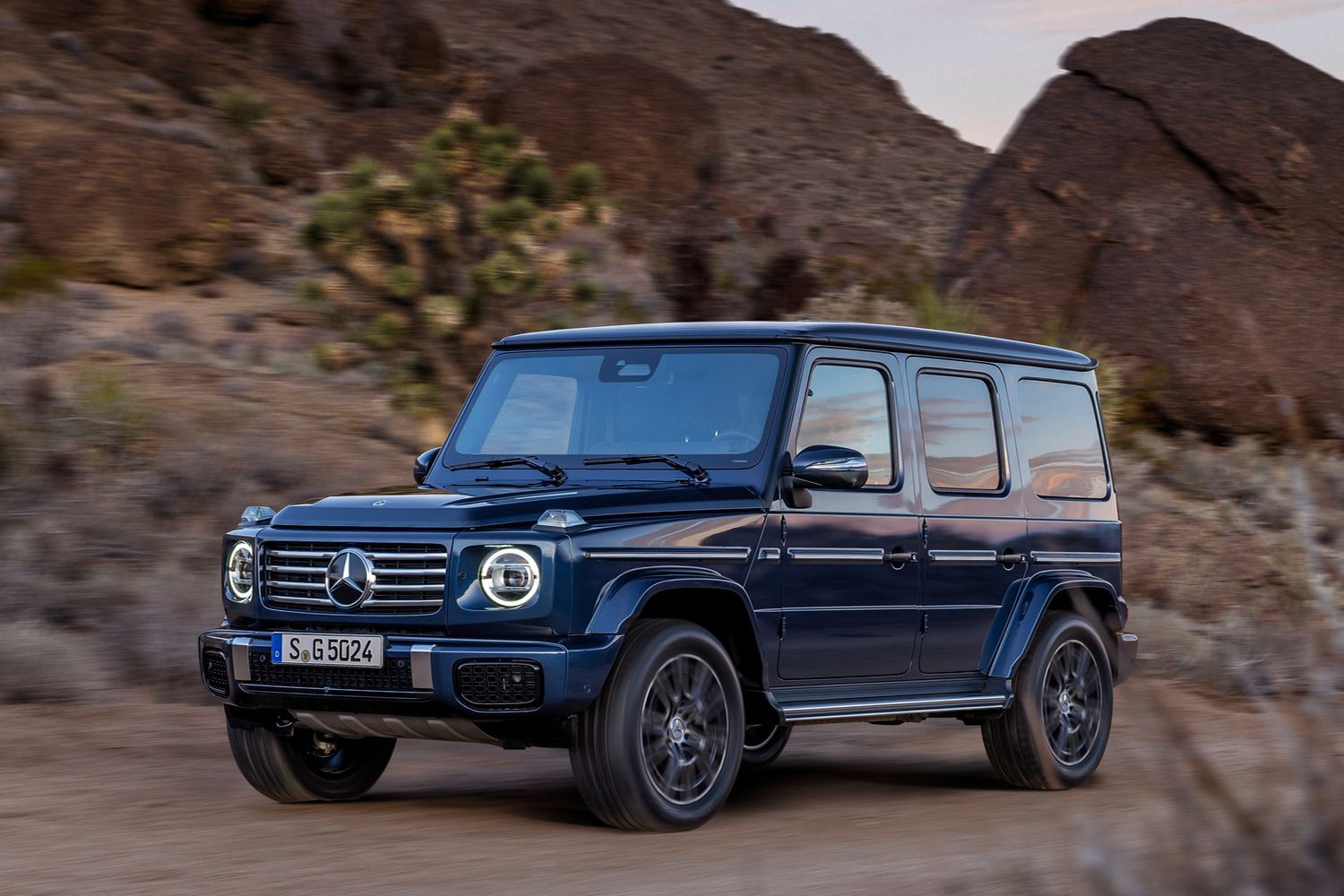 Side view of a dark blue Mercedes-Benz G-Class driving in the desert.