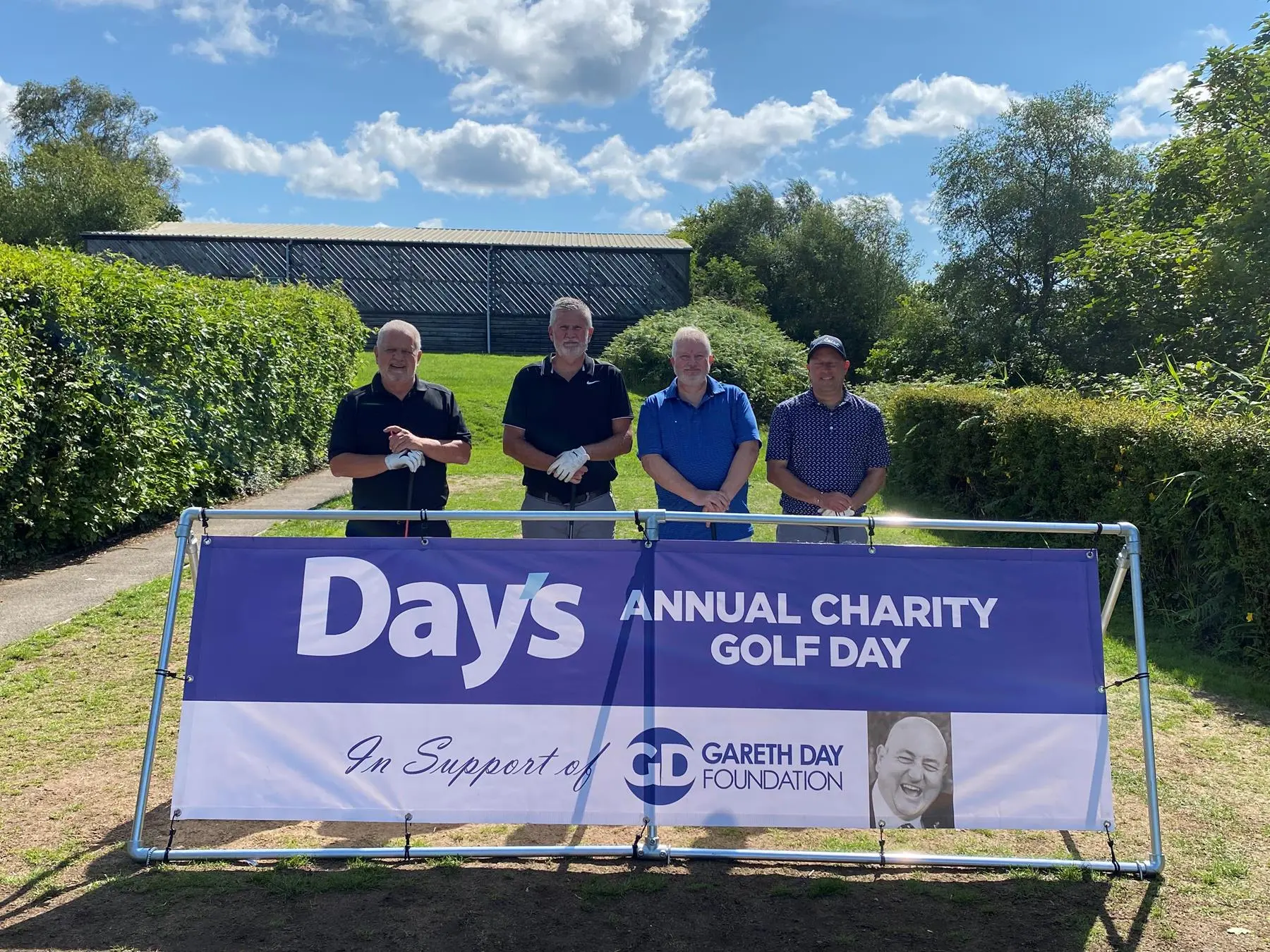 4 Men stood in front of Day's Annual Charity Golf Day banner