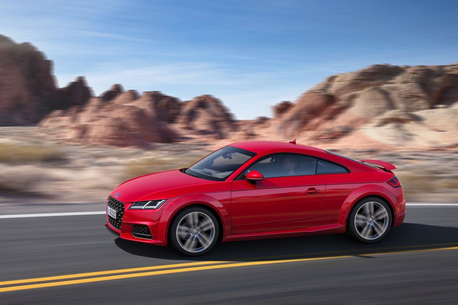 New Audi TT Coupe in red, image of vehicle driving on a road from the side view