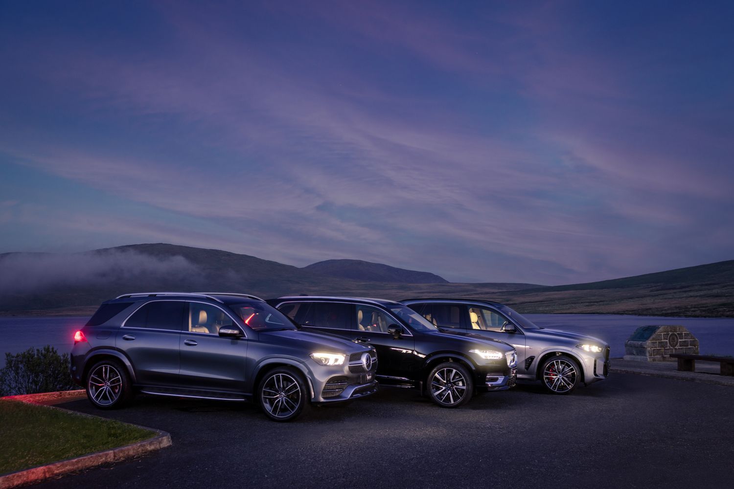 Front and side view of three latest SUV models available at Agnew (Mercedes-Benz GLC, Q4 e-tron and a BMW X4), parked at scenic car park next to lake during sunrise.