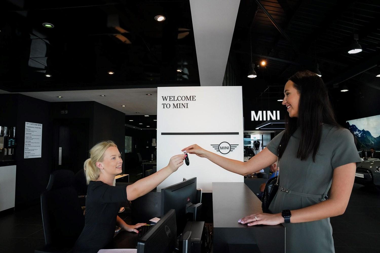 MINI Sales Specialist hands over new car keys to customer at the Bavarian MINI Showroom reception