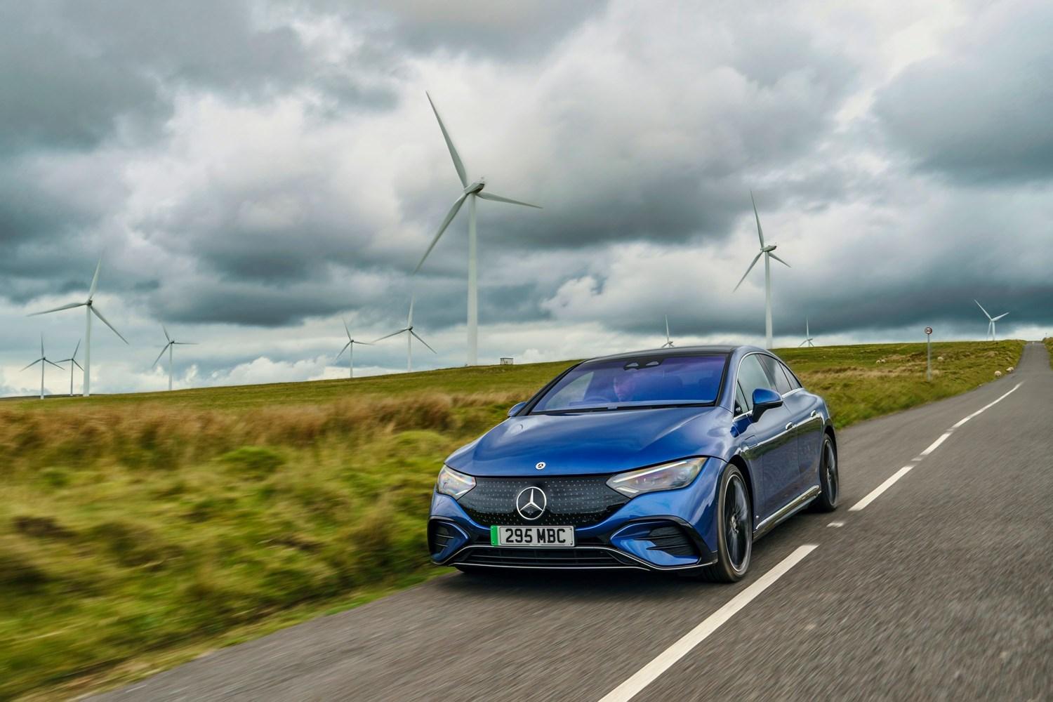 Mercedes-Benz EQE in blue, drives along country road with windmills in the background