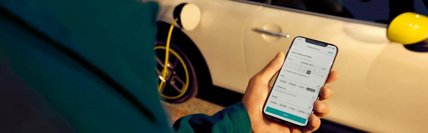 Close-up of MINI customer using the MINI Connected App on mobile with MINI Electric charging in the background.
