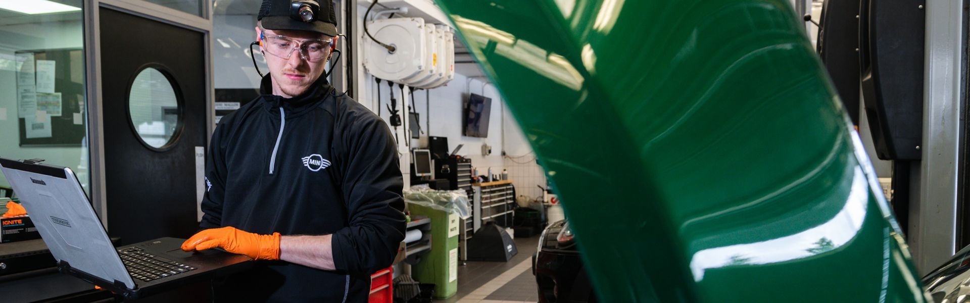 MINI Repair Specialist checks the electrics of a MINI Countryman on laptop while looking at the engine at the MINI Repair Centre in Bavarian MINI