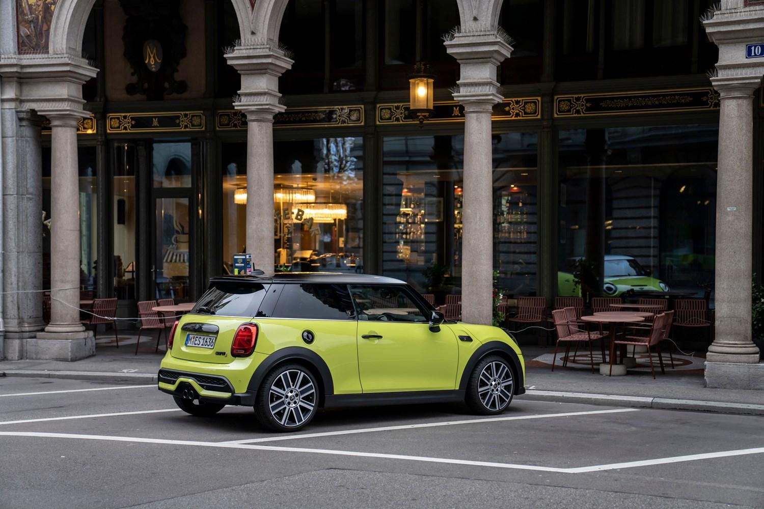 Rear view of the new MINI 3-Door Hatchback in yellow, parked in car park space next to old building with shops in European city