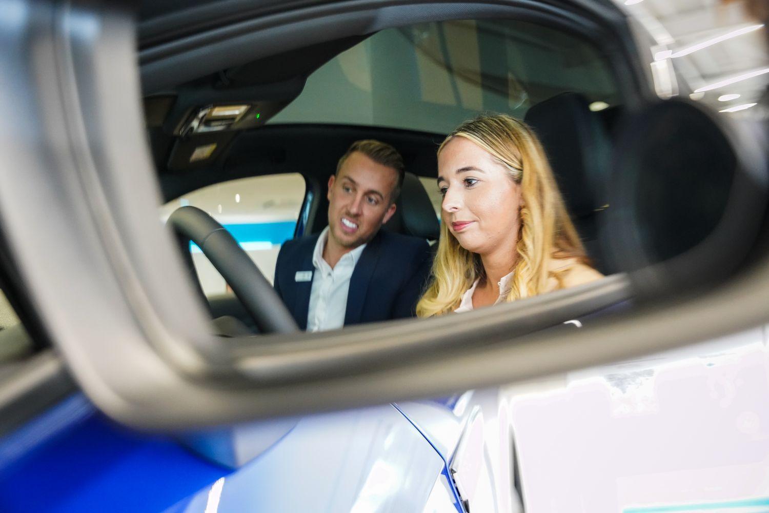Volkswagen Sales Advisor chats to customer about Volkswagen vehicle whilst they both sit inside