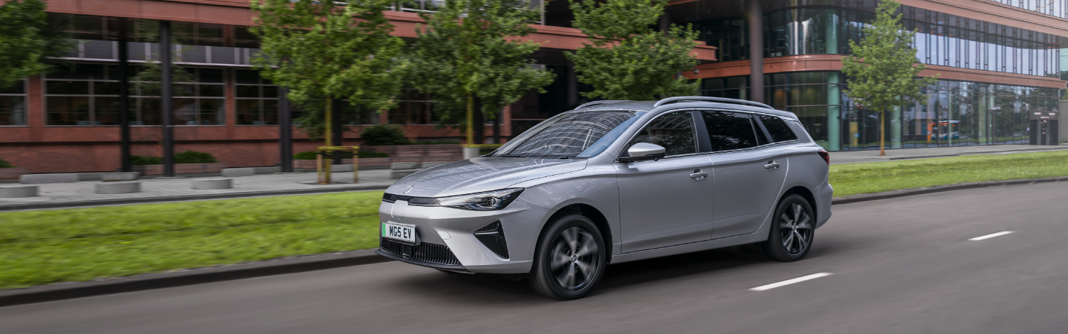 Three quarter view of a Silver MG5 EV on a city road in motion, on a gloomy day