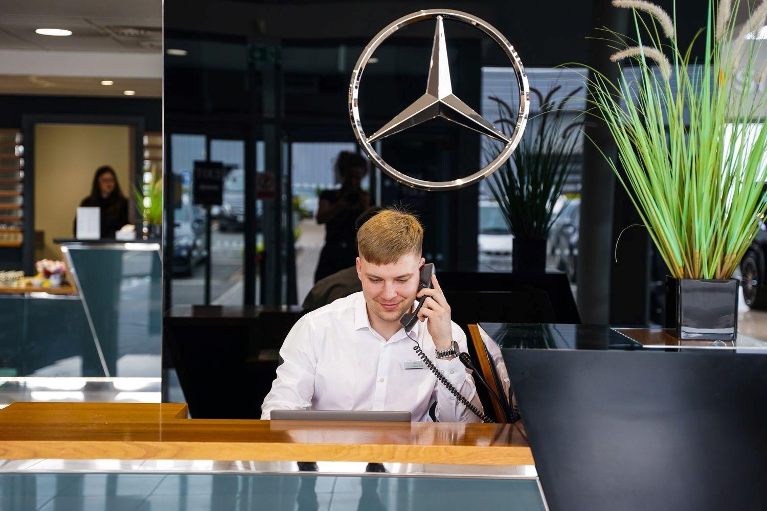 Mercedes-Benz Customer Service Specialist answers customer phone call in the Mercedes-Benz of Belfast showroom