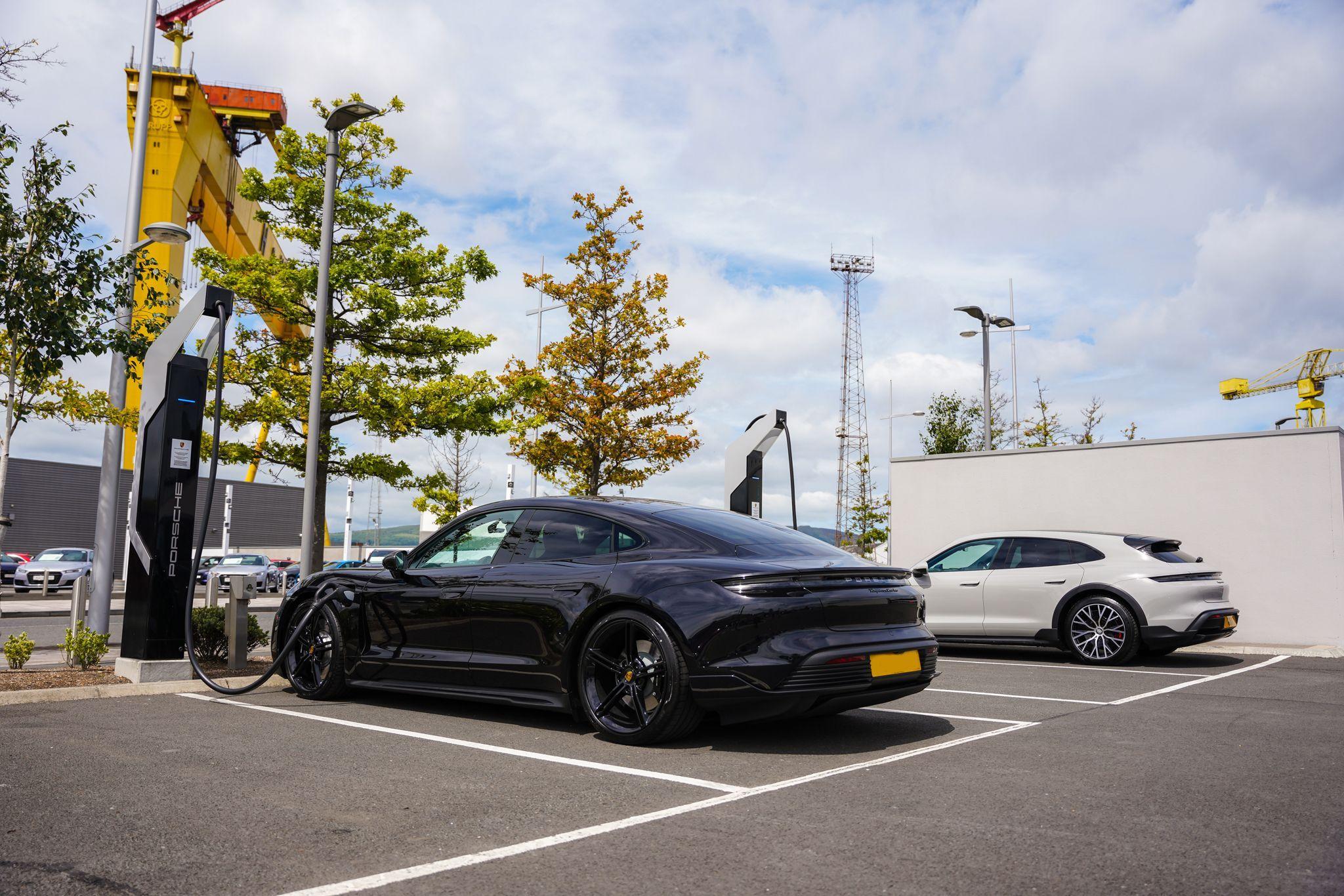 Two Porsche Panameras charging at the electric charging points at Porsche Centre Belfast with the Harland and Wolff cranes behind.