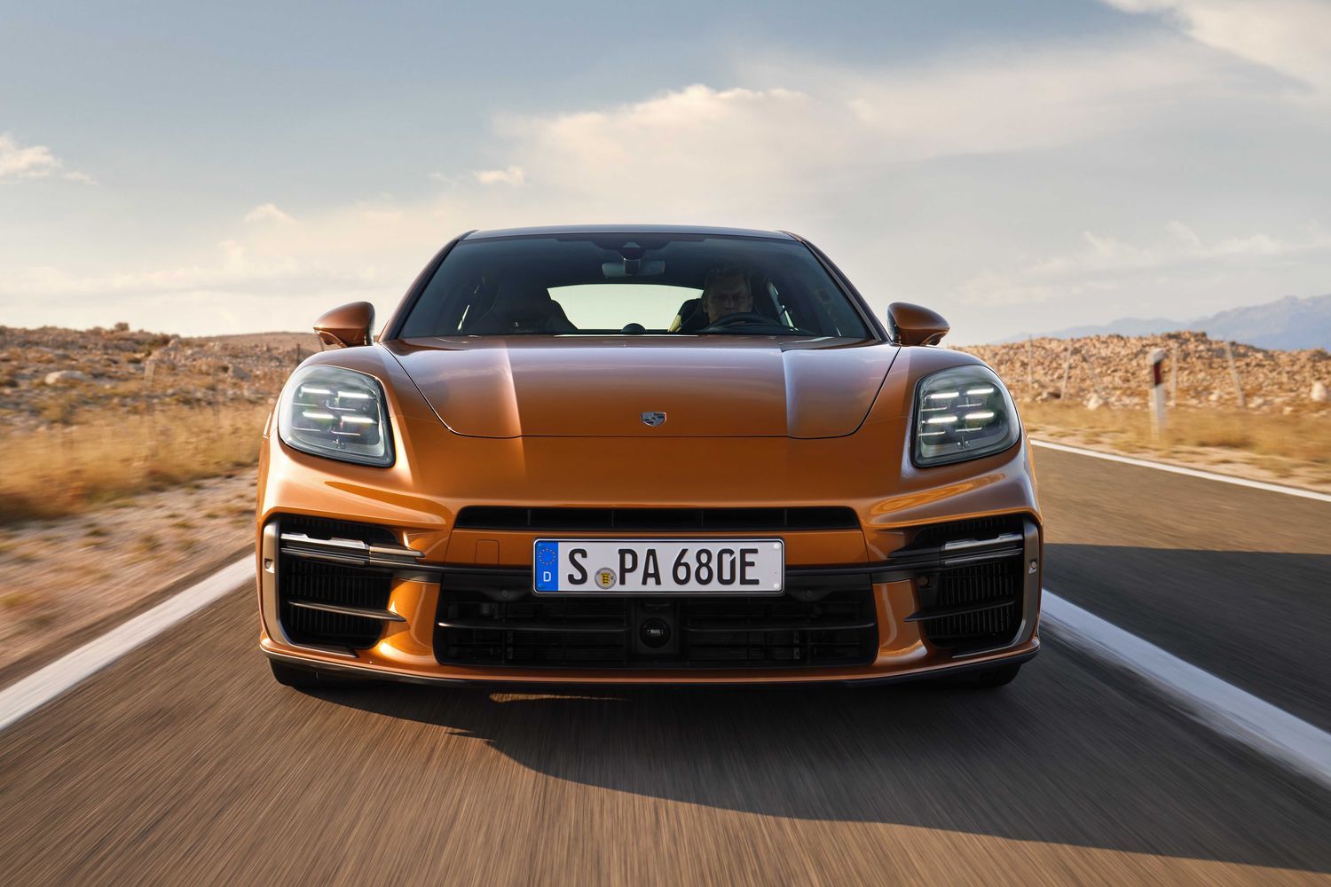 Front view of the new Porsche Panamera in orange, driving along desert road