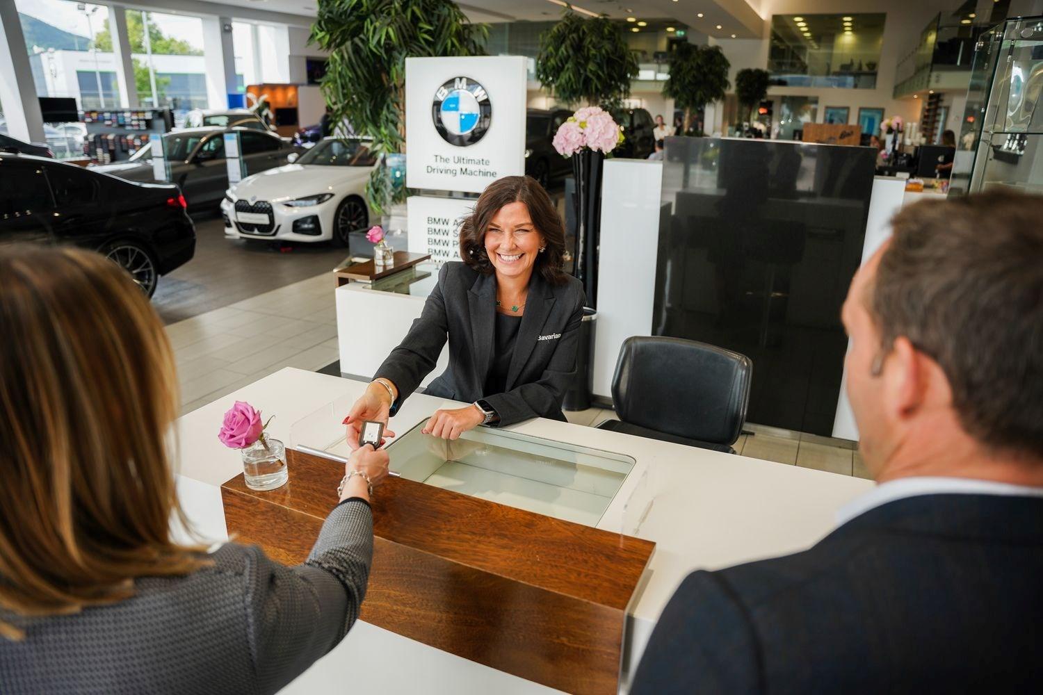 BMW Sales Specialist smiles as they hand over new car keys to customers who have just bought a new BMW vehicle at the Bavarian BMW Belfast showroom