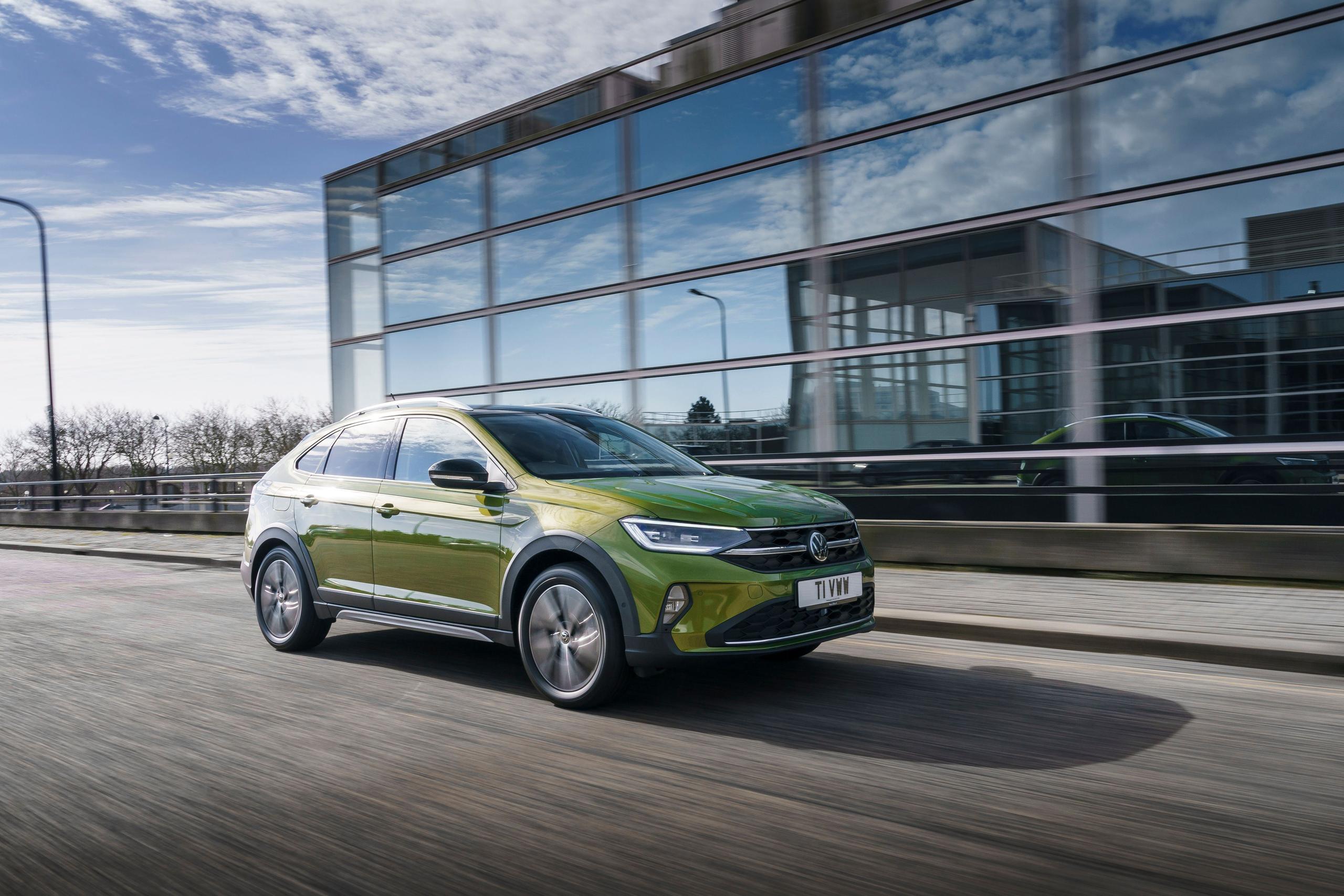 Side view of the new Volkswagen Taigo in green, driving on street past modern building