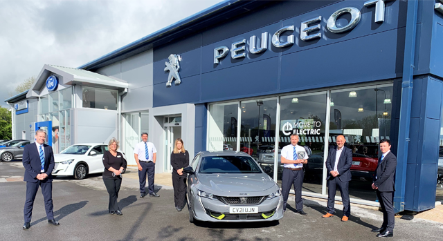 Employees standing outside of Peugeot dealership with Silver Peugeot