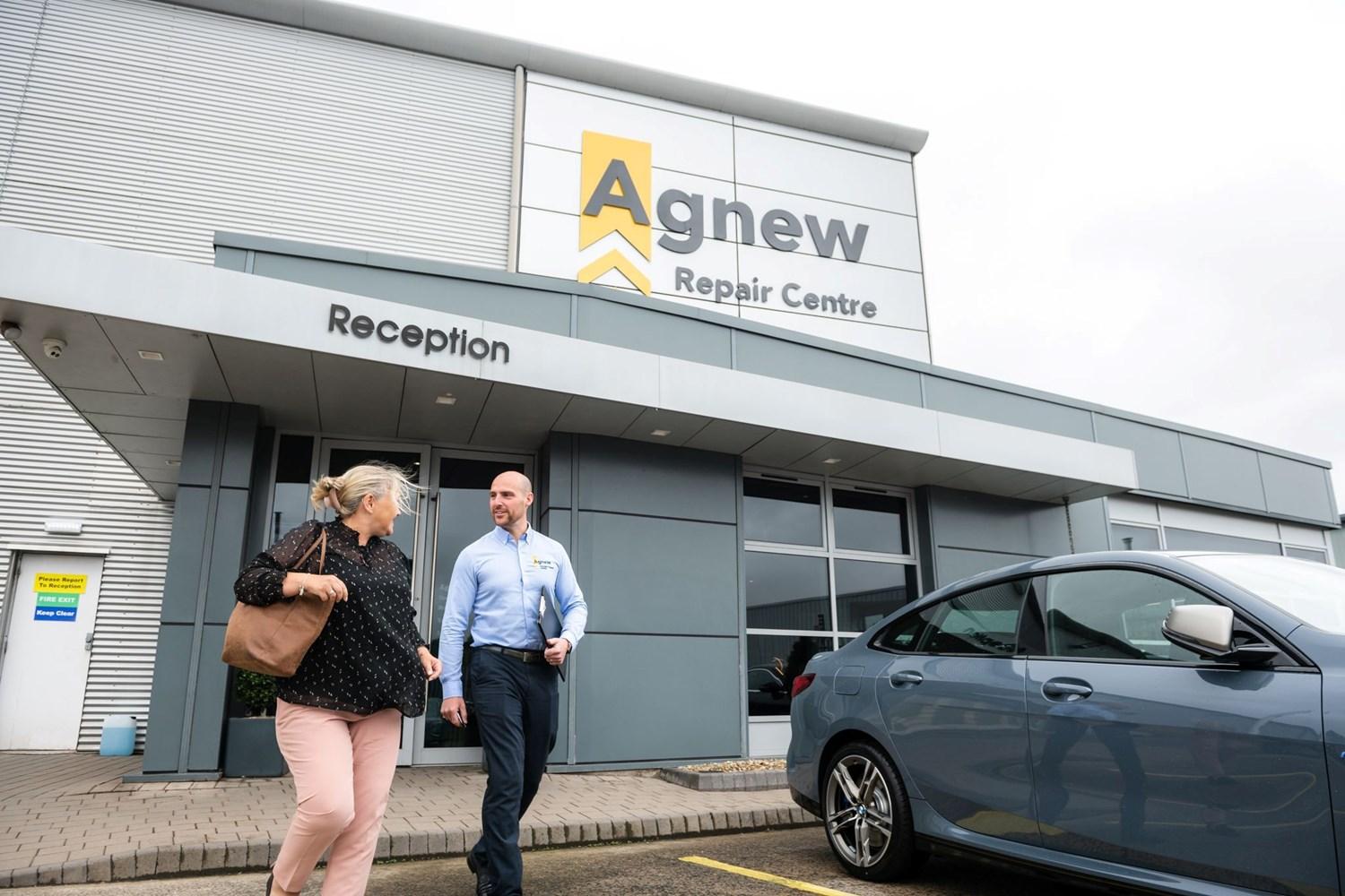 Vehicle Damage Assessor talks to customer about repairs to be made to vehicle outside the main reception entrance of Agnew Repair Centre, Belfast, Northern Ireland.