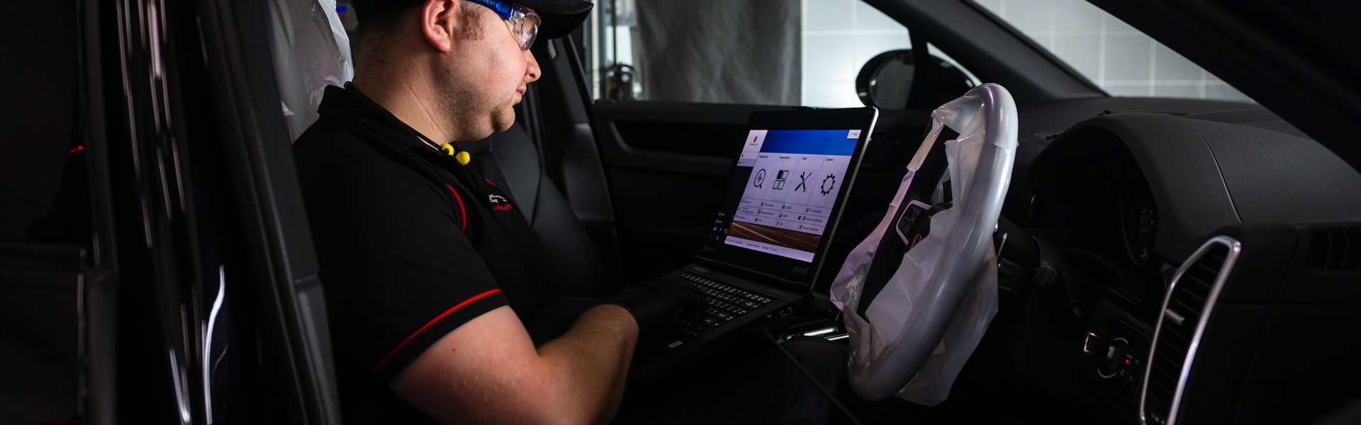 Porsche Centre Belfast Repair Specialist sits in the inside of Porsche vehicle as they inspect the electrics on laptop.