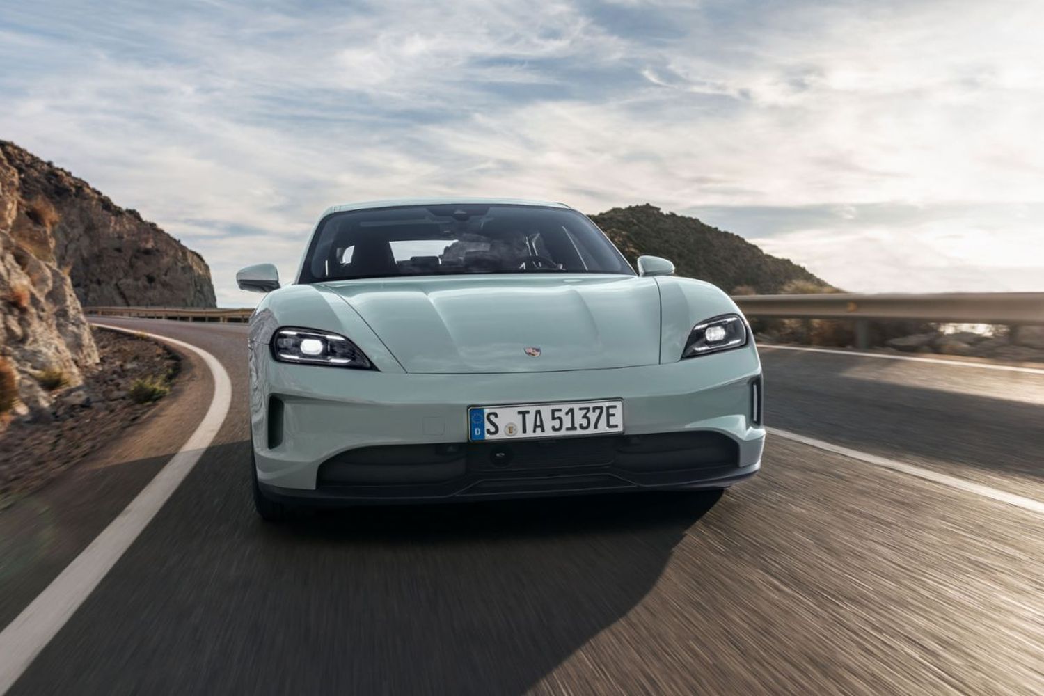 Front view of the new Porsche Taycan in white, driving along cliff edge