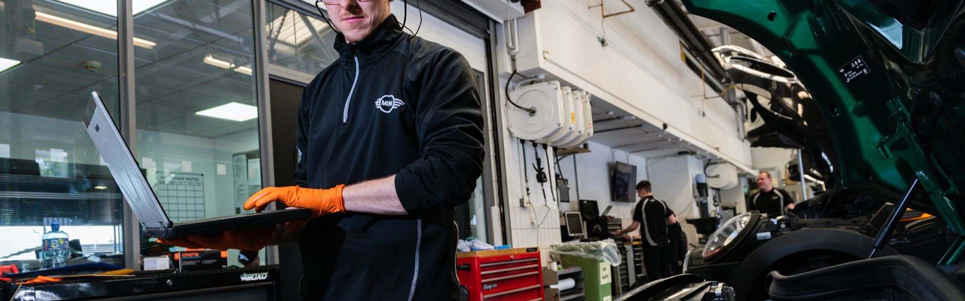 MINI Repair Specialist checks electrics of car on laptop while looking at the engine of a MINI Countryman at the MINI Repair Centre at Bavarian MINI