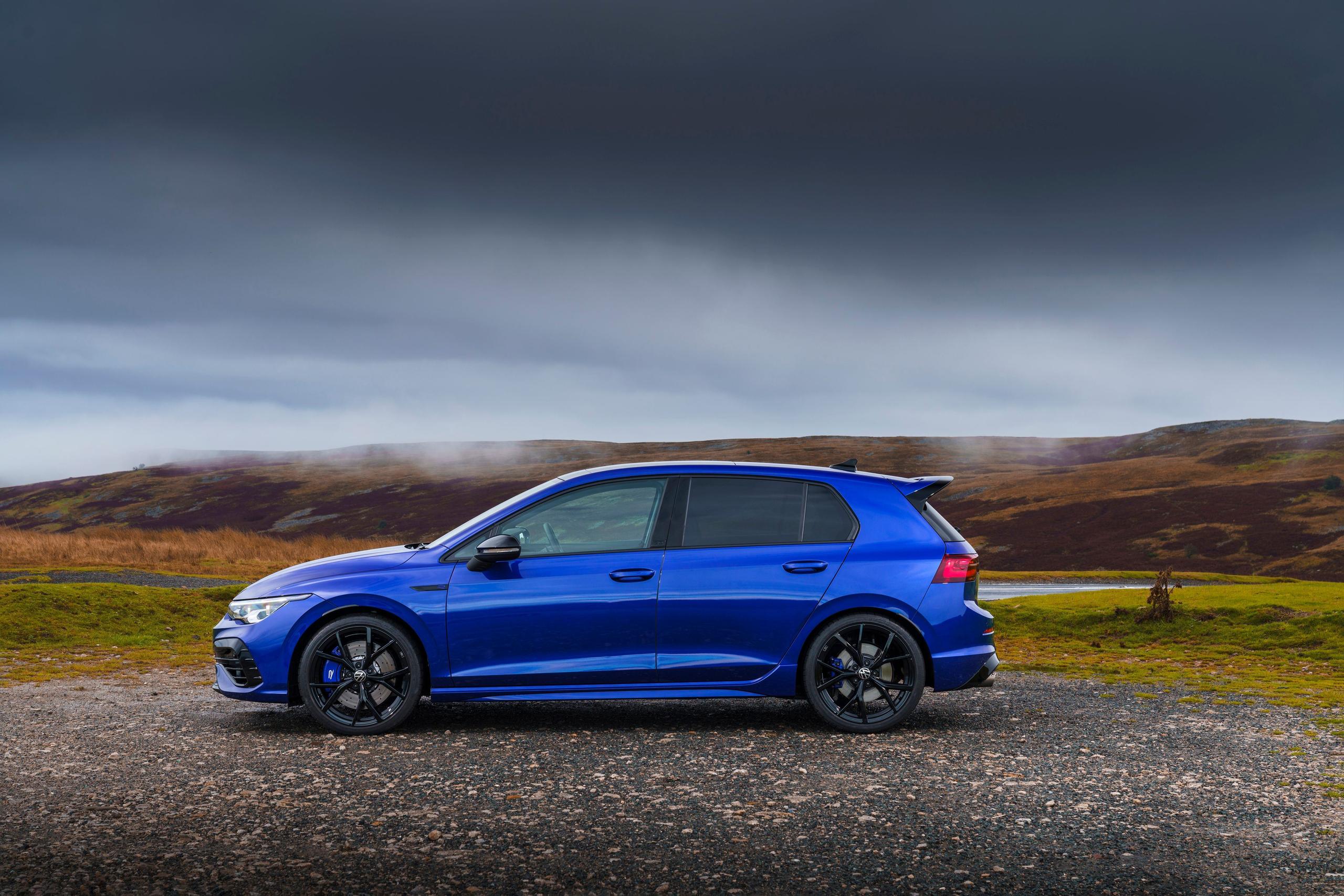 Side view of the new Volkswagen Golf in blue, parked to the side of country road with mountains and lake behind