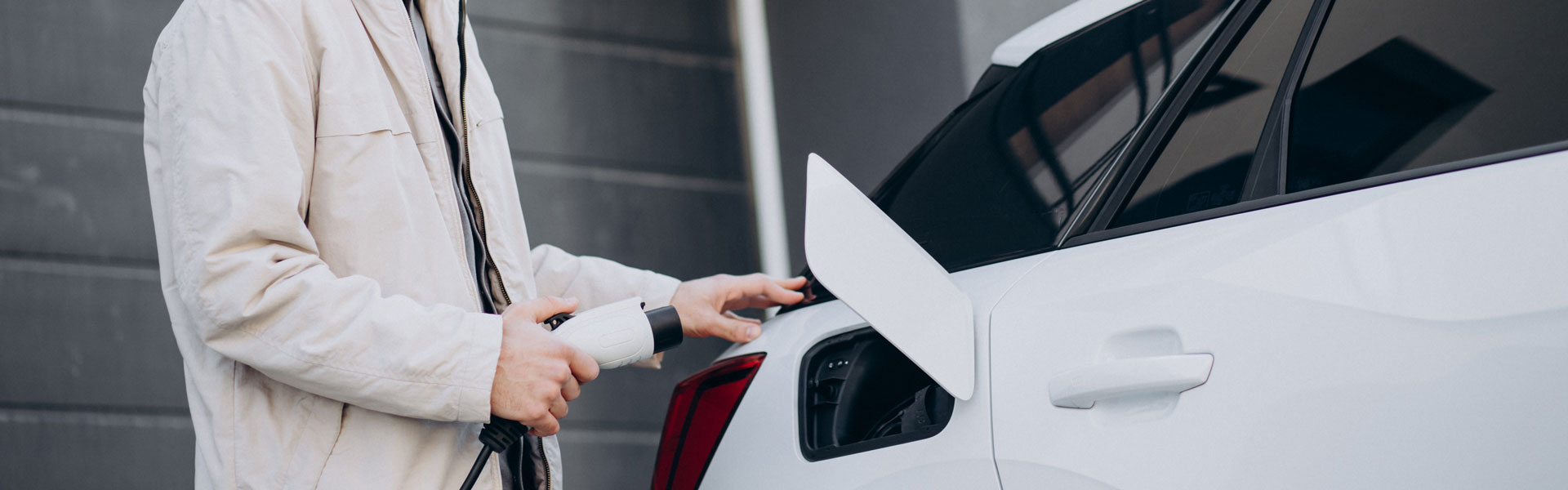 Person plugs vehicle into an electric charging station in car park