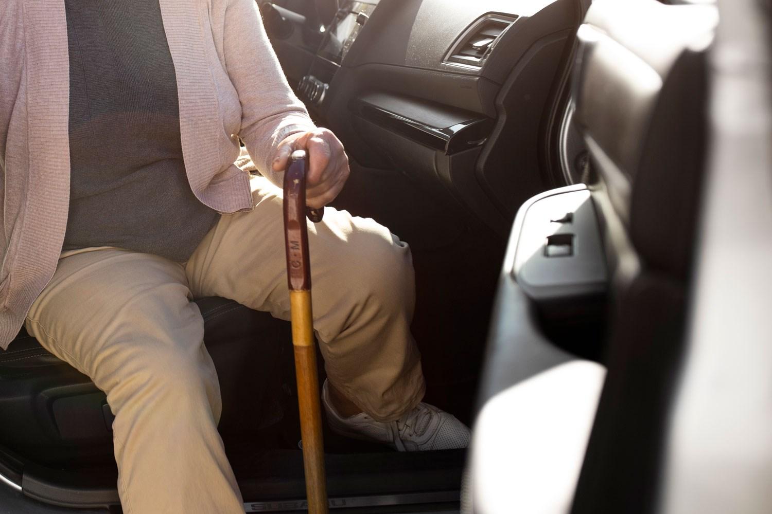 Elderly person uses walking aid to get out of the passenger side of a vehicle