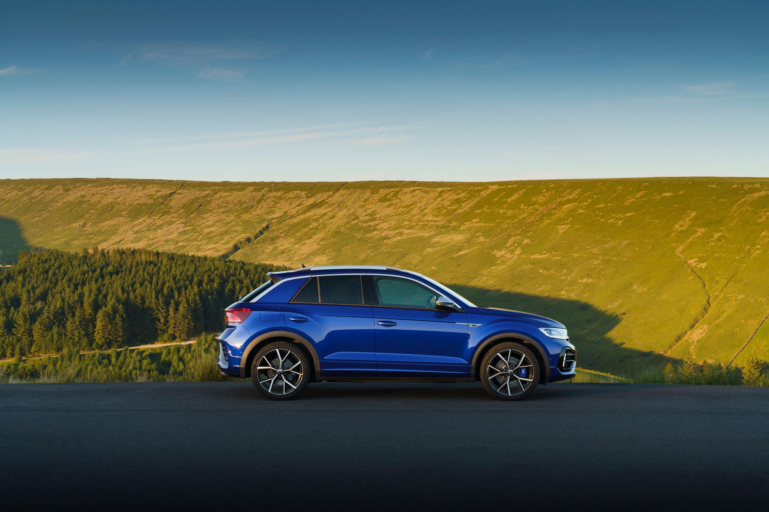 Side view of the new Volkswagen T-Roc in blue, parked on country road next to forest and hills