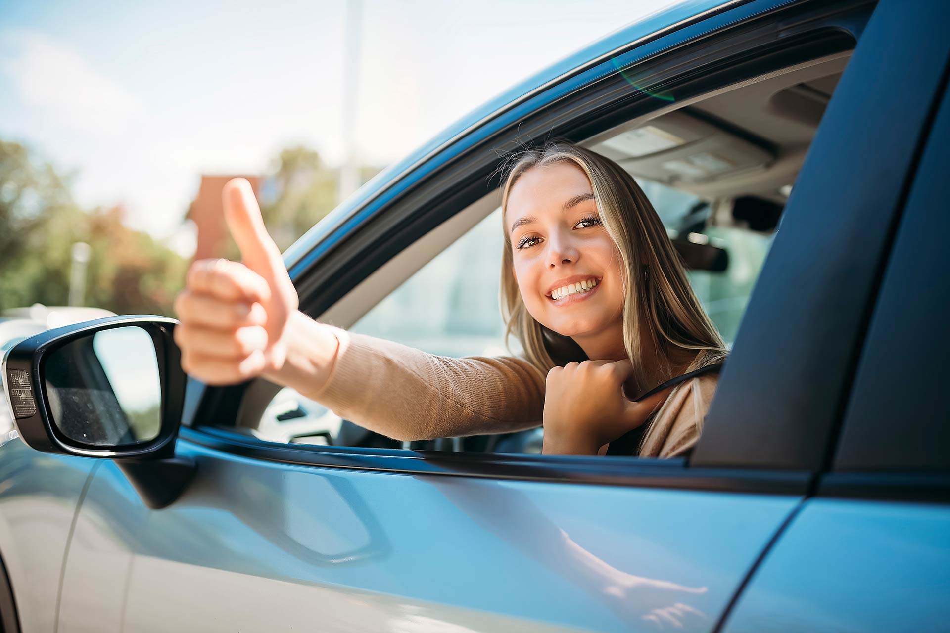 Woman sat in car leaning out of window giving thumbs up. 