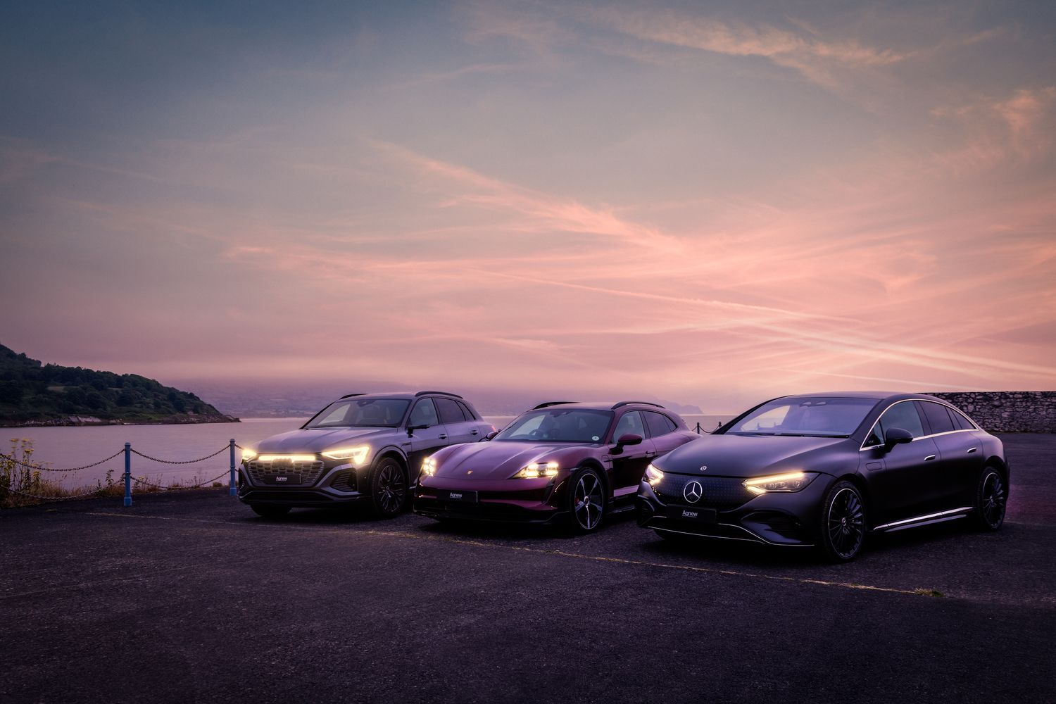 Audi Q3, in black, Porsche Macan, in red and Mercedes-Benz EQE are parked in a coastal car park by the sea during sunset