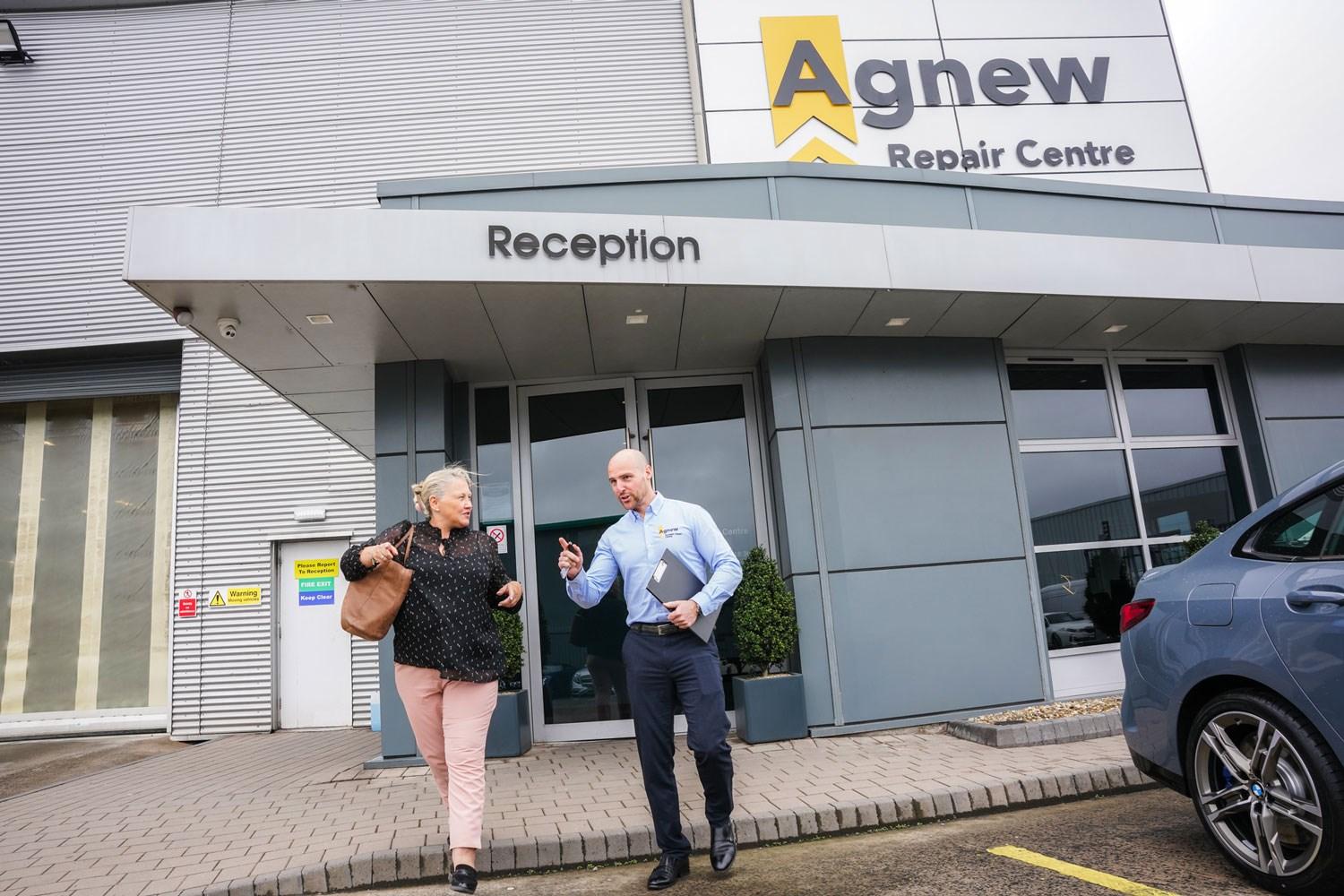 Vehicle Damage Assessor talks to customer as they walk towards their car for assessment. Behind them, is the reception of the Agnew Repair Centre, Belfast, Northern Ireland.