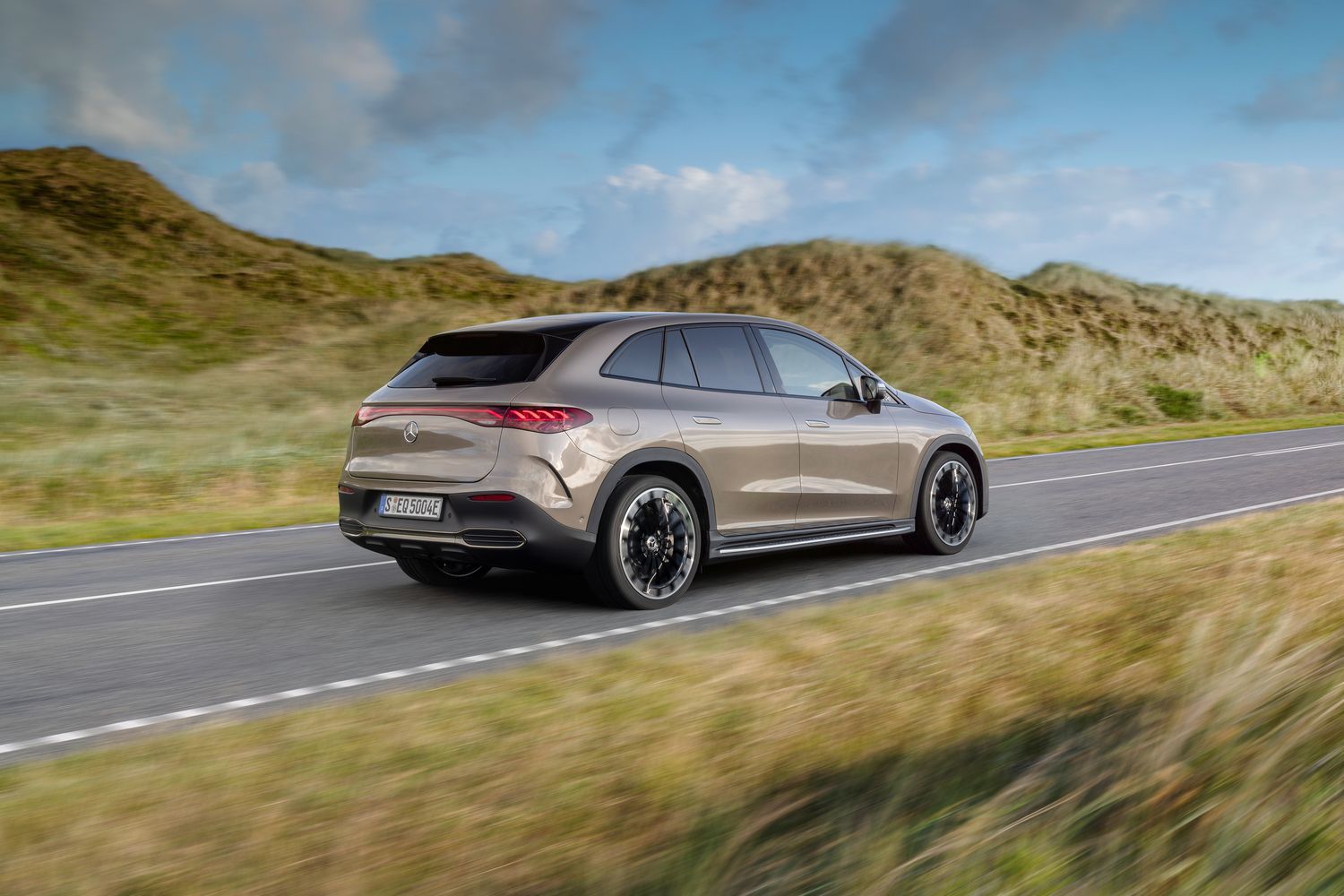 Rear end view of a brown EQE SUV driving.