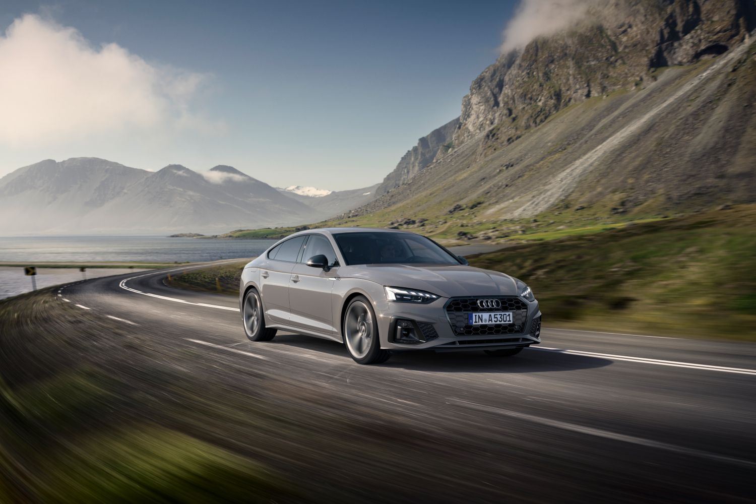 New Audi A5 Sportback driving outdoors showcasing the sporty headlights and front grill.