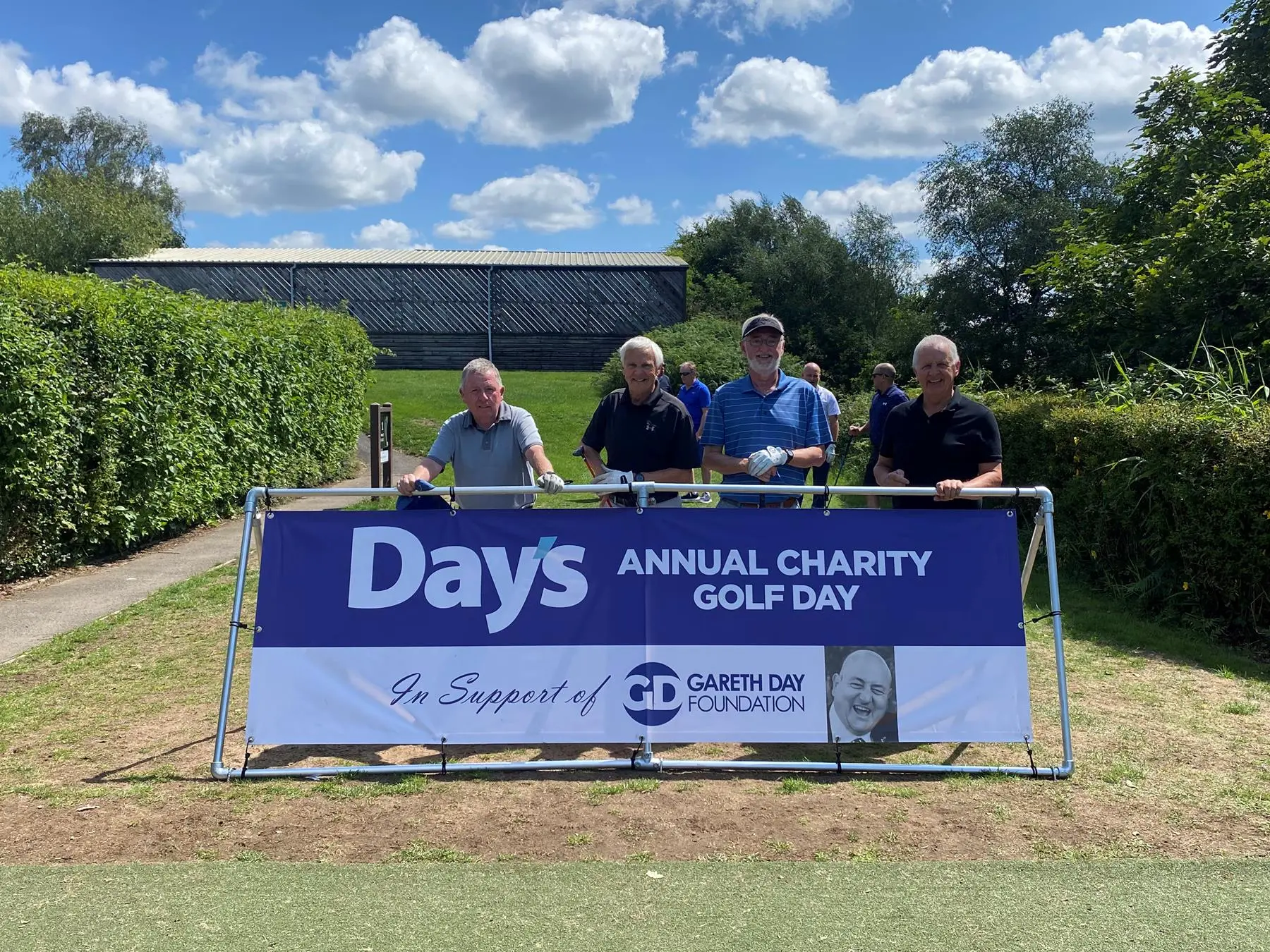 4 Men stood in front of Day's Annual Charity Golf Day banner