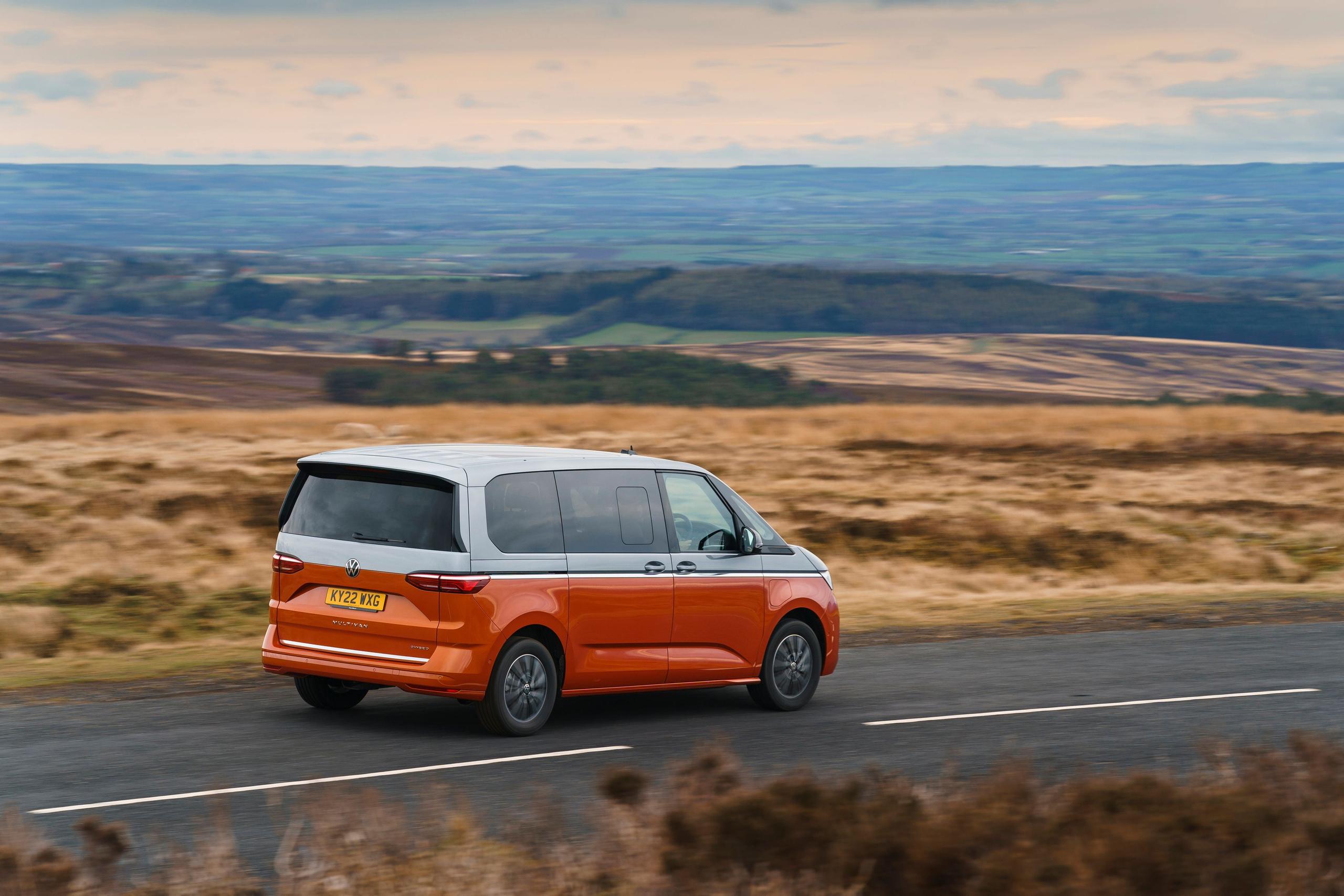 Rear and side view of the new Volkswagen Multivan in orange, driving along country road