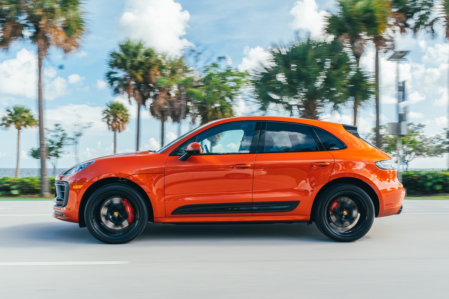 Side view of the new Porsche Macan in orange, driving along road with palm trees behind